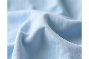 Tekstur kain linen biru muda yang ringan dan bertekstur, ideal untuk iklim tropis.